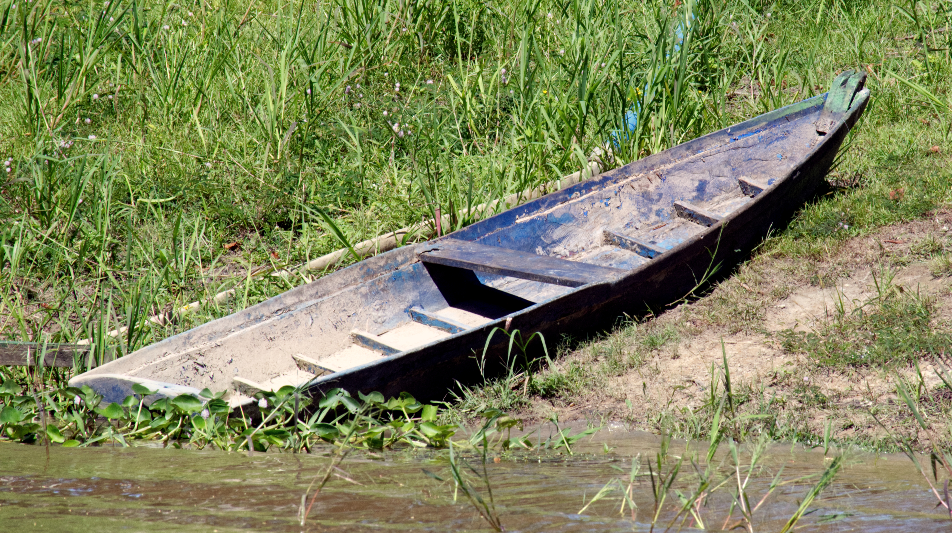 Mud clings to a canoe pulled onto the bank, settling as the water’s motion slows. The rise and fall of the river shifts the boundary between river and land, wherein sediment is deposited and disturbed with each change in level. Surfaces retain these traces, showing recent interaction with the river.